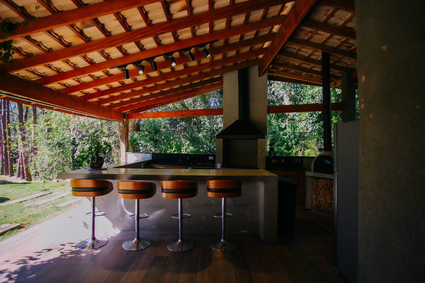 Área gourmet da Casa Lago com churrasqueira, balcão e banquetas de madeira