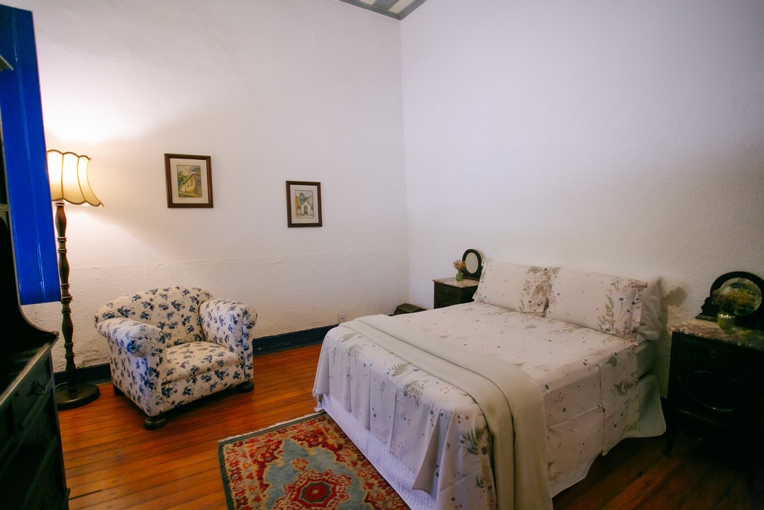 Quarto da Casa Sede com poltrona e piso de madeira