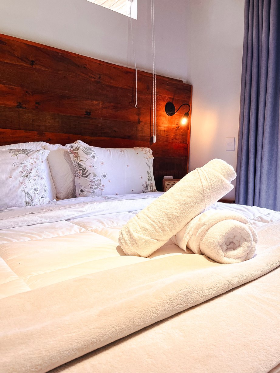 Detalhe de uma suíte com enxoval branco e toalhas dobradas sobre a cama
